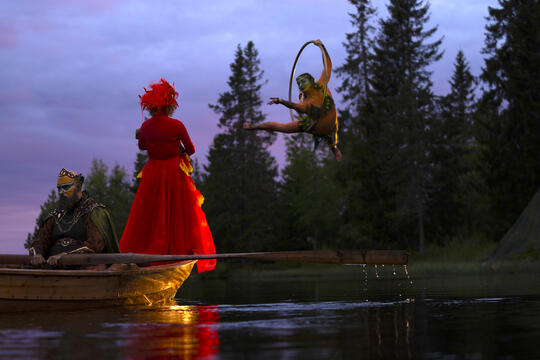 Rødkledd kvinne står i båt mens et vesen svever i en ring over vannet
