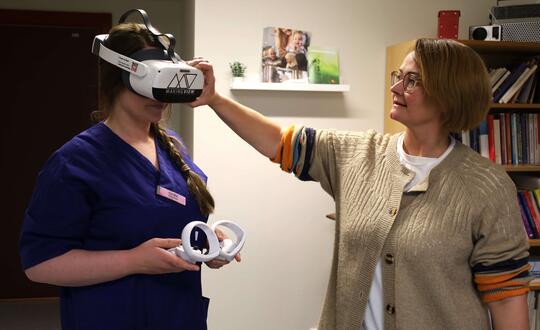 dame med VR-briller og ei dame som sjekker at de sitter ordentlig på