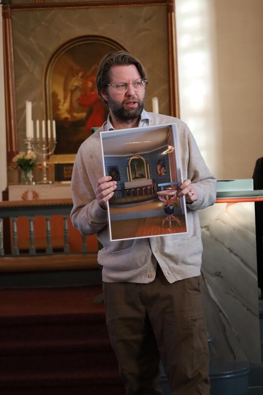 mann som står foran et alter og holder opp et bilde