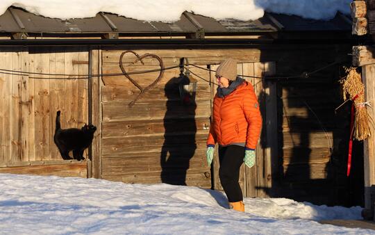 dame i oransje boblejakke lokker på katt foran tømmerhus