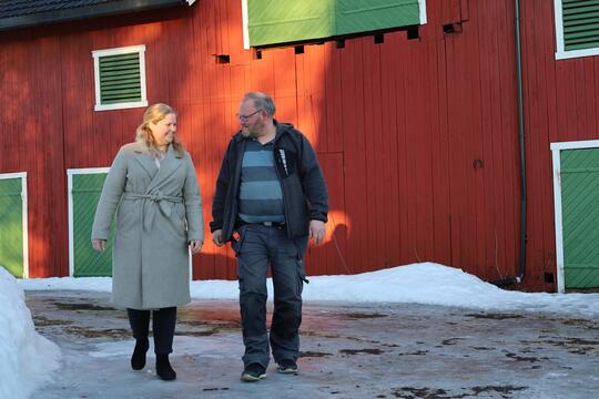 mann og dame går på isen foran rød låve med grønne dører